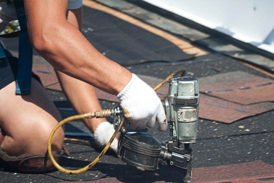 Man using nail gun to position roof shingles properly.