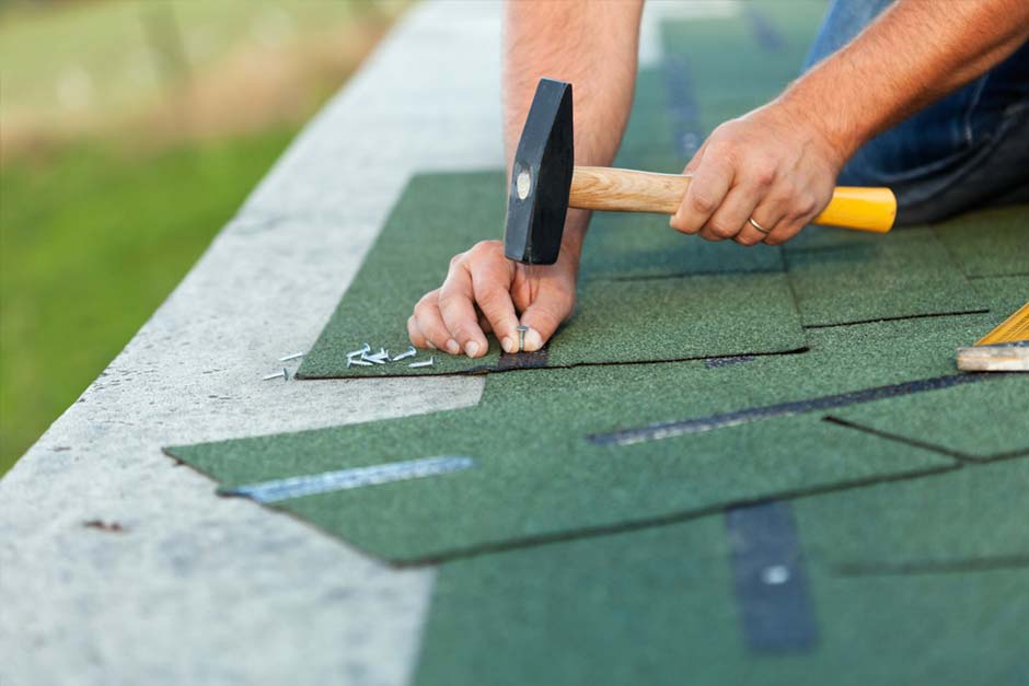 man using a hammer and nails to fix roof shingles