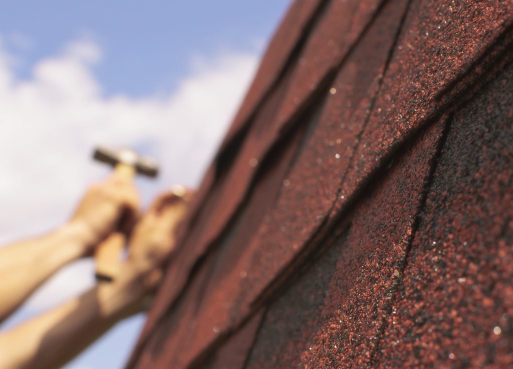 unfocused hands repairing a roof with red shingles in the forefront, focused
