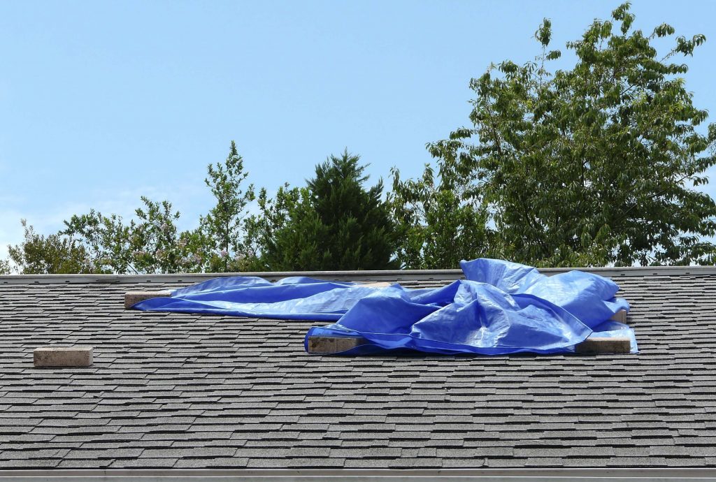 picture of roof wind damage covered by a tarp held down with rocks