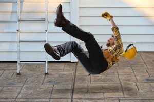 Man with hard hat being careless falling from ladder onto concrete floor