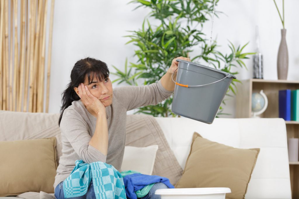 A woman holding a grey bucket up to catch water from a roof leak in El Paso.