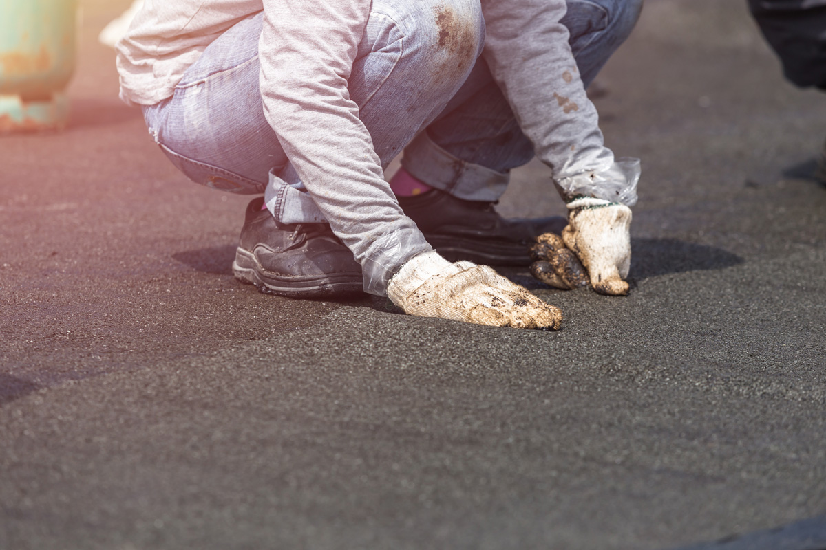 A person performing maintenance on a black, flat roof in El Paso.